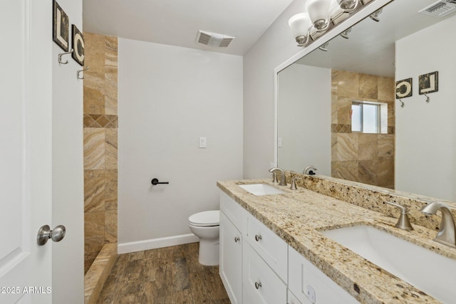 bathroom with hardwood / wood-style flooring, toilet, vanity, and a tile shower