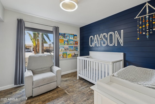 bedroom with wood walls, dark hardwood / wood-style floors, and a nursery area