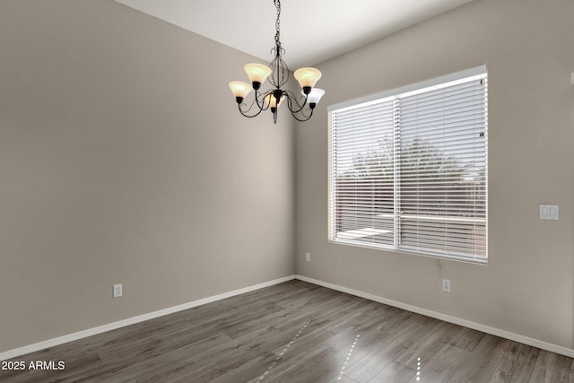 empty room featuring wood-type flooring and an inviting chandelier