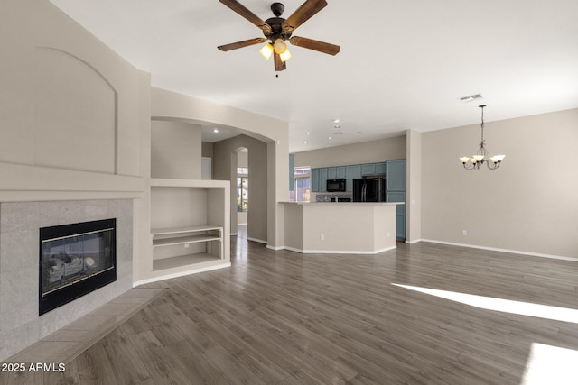 unfurnished living room with built in features, dark hardwood / wood-style flooring, ceiling fan with notable chandelier, and a tile fireplace