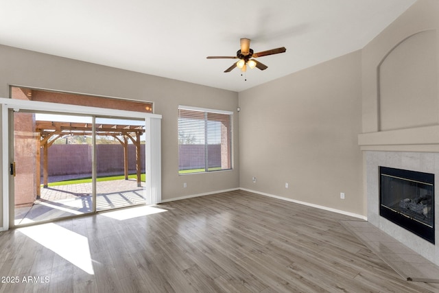 unfurnished living room featuring hardwood / wood-style flooring, ceiling fan, and a tiled fireplace