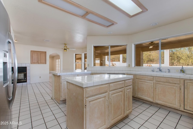 kitchen with ceiling fan, tile countertops, a center island, and light brown cabinets