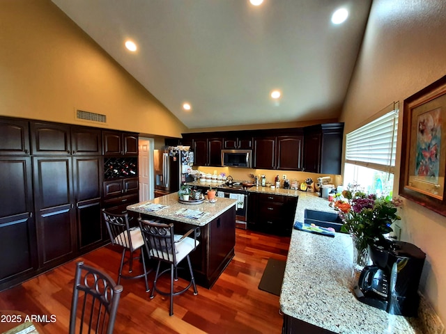 kitchen with high vaulted ceiling, a center island, stainless steel appliances, light stone countertops, and visible vents