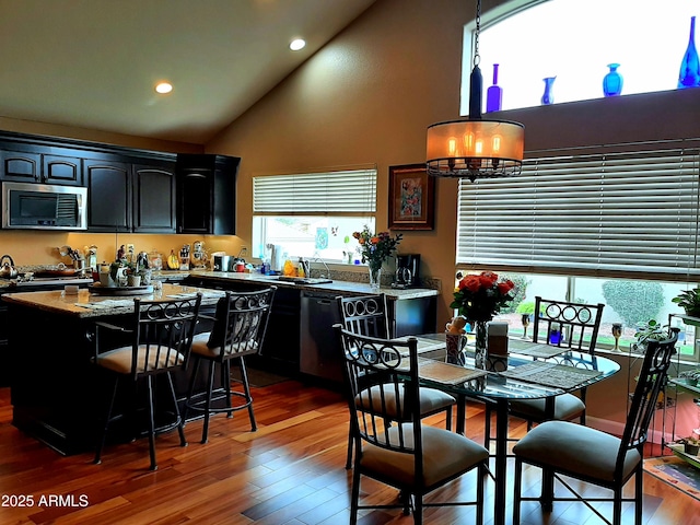 kitchen featuring stainless steel microwave, recessed lighting, wood finished floors, a kitchen island, and high vaulted ceiling