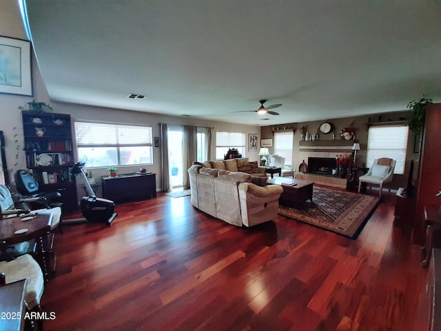 living area featuring a ceiling fan, a healthy amount of sunlight, wood finished floors, and a tiled fireplace