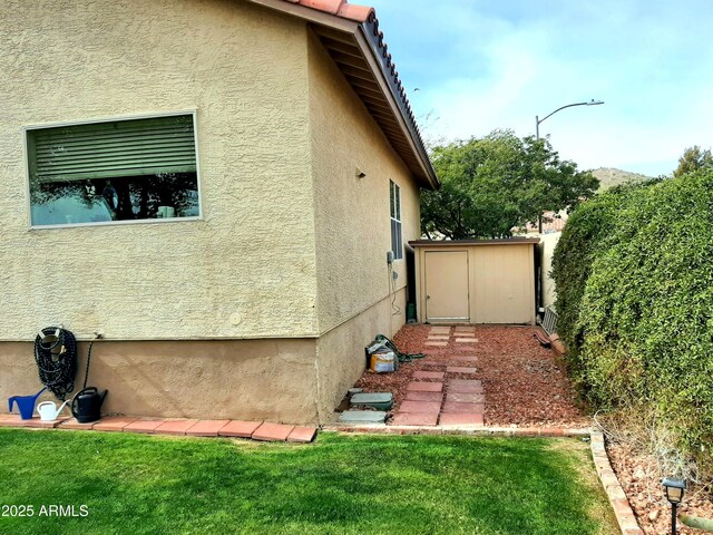 view of side of property featuring an outbuilding, a storage unit, and stucco siding