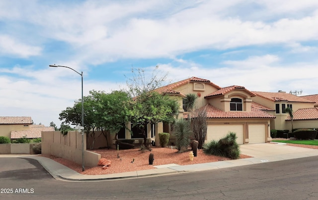 mediterranean / spanish house featuring stucco siding, a tiled roof, concrete driveway, and fence