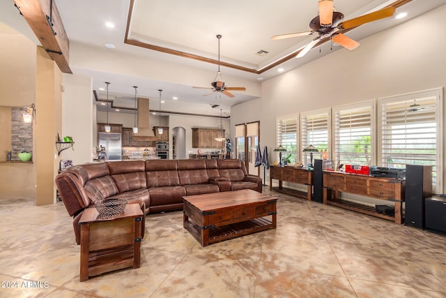 living room with a raised ceiling, crown molding, a towering ceiling, and ceiling fan