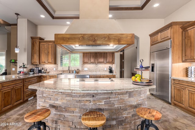 kitchen with light stone counters, appliances with stainless steel finishes, a breakfast bar, and custom range hood