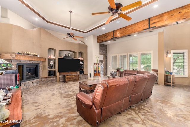 living room with a stone fireplace, a towering ceiling, built in features, ceiling fan, and a tray ceiling