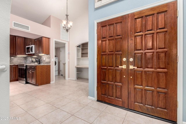 entryway featuring washer / clothes dryer, high vaulted ceiling, light tile patterned floors, a chandelier, and baseboards