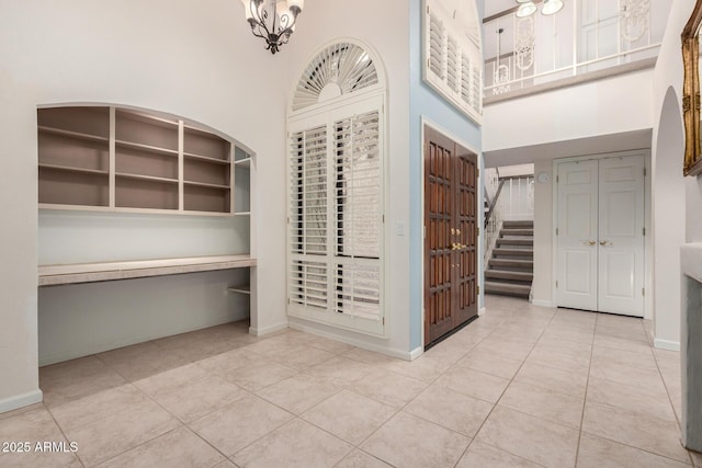 tiled entryway with a high ceiling, baseboards, and a chandelier