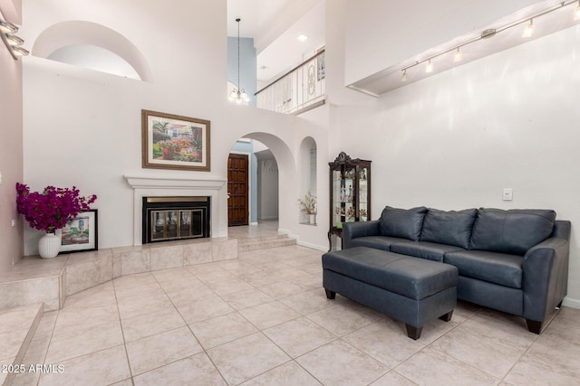 living room with arched walkways, baseboards, light tile patterned flooring, a high ceiling, and a glass covered fireplace