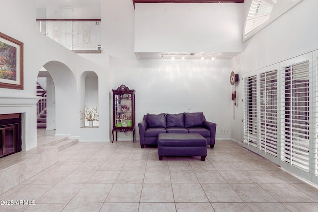 living room featuring a towering ceiling, light tile patterned floors, baseboards, and a fireplace