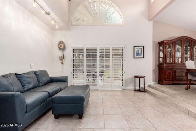 living area with light tile patterned floors, a towering ceiling, track lighting, and baseboards