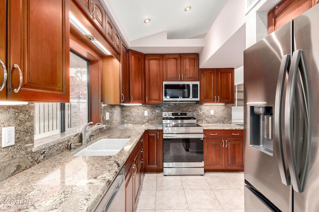 kitchen with appliances with stainless steel finishes, a sink, light tile patterned floors, light stone counters, and decorative backsplash