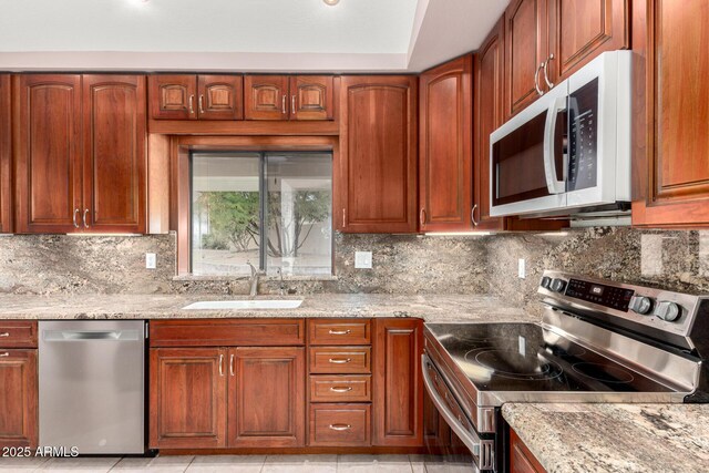 kitchen featuring appliances with stainless steel finishes, a sink, light stone counters, backsplash, and light tile patterned floors