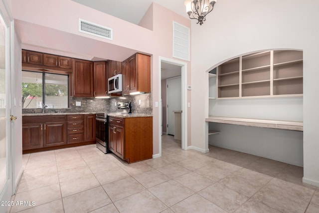 kitchen with stainless steel electric range oven, white microwave, a sink, light stone countertops, and light tile patterned floors