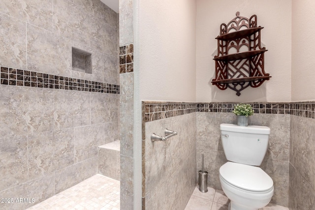 full bath featuring toilet, a tile shower, tile walls, and tile patterned flooring