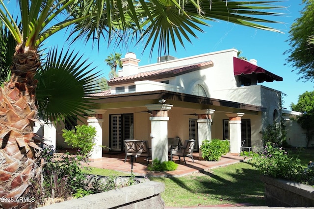 rear view of property with stucco siding, a chimney, a ceiling fan, and a patio area