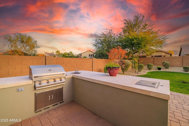 patio terrace at dusk featuring a grill and an outdoor kitchen