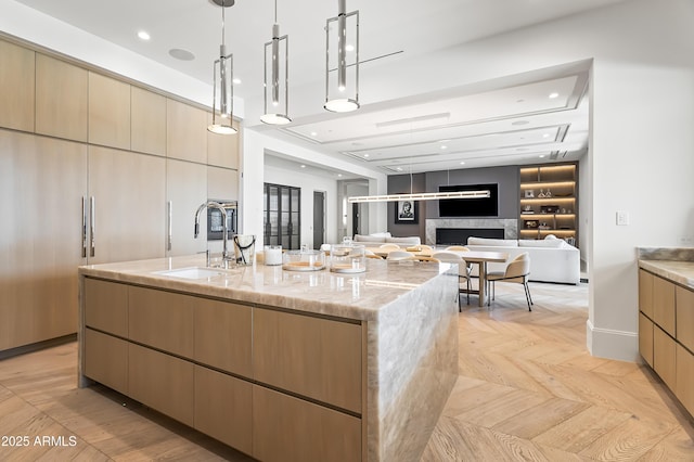 kitchen with sink, a center island with sink, pendant lighting, light stone countertops, and light parquet floors