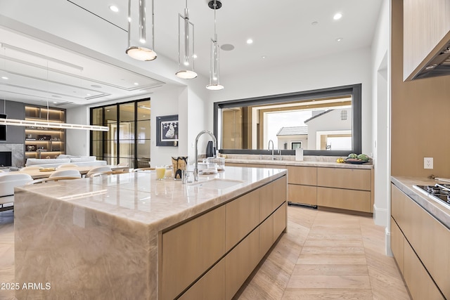 kitchen featuring a large island, sink, light parquet floors, light stone countertops, and decorative light fixtures