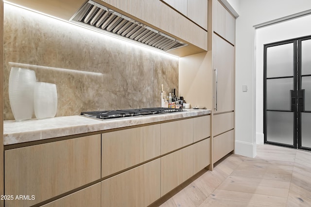 kitchen featuring wall chimney exhaust hood, stainless steel gas cooktop, and light brown cabinets