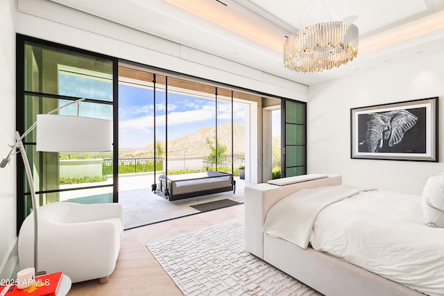 bedroom featuring a chandelier, access to outside, a raised ceiling, a mountain view, and light hardwood / wood-style floors