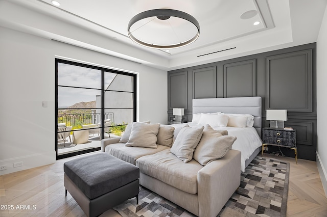 bedroom featuring access to outside, a raised ceiling, and light parquet flooring