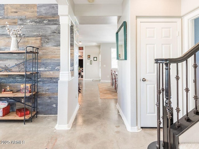 hallway featuring concrete flooring, stairway, and baseboards