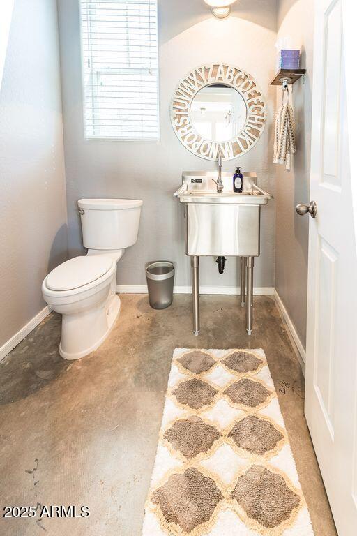 half bathroom featuring concrete flooring, toilet, and baseboards