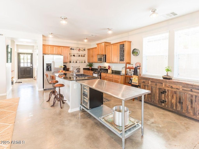 kitchen with stainless steel appliances, a sink, visible vents, a kitchen bar, and finished concrete floors