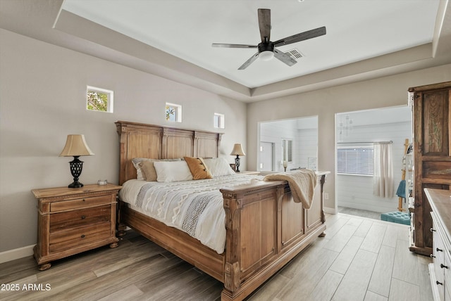 bedroom featuring multiple windows, ceiling fan, light hardwood / wood-style floors, and a tray ceiling