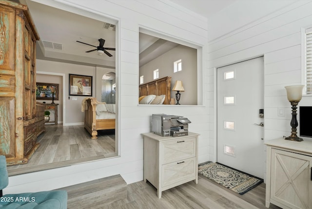 foyer with wooden walls, visible vents, ceiling fan, and light wood-style flooring