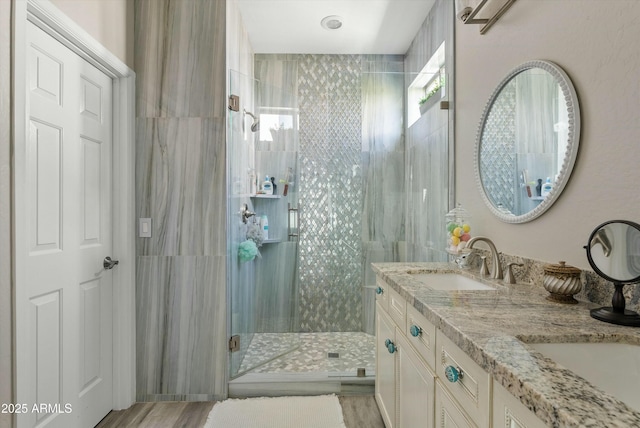 full bathroom with double vanity, wood finished floors, a sink, and a shower stall