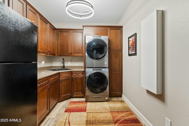 clothes washing area featuring cabinets, stacked washer / drying machine, sink, and light wood-type flooring