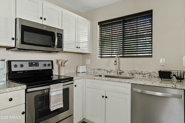 kitchen with stainless steel appliances, white cabinetry, a sink, and light stone counters