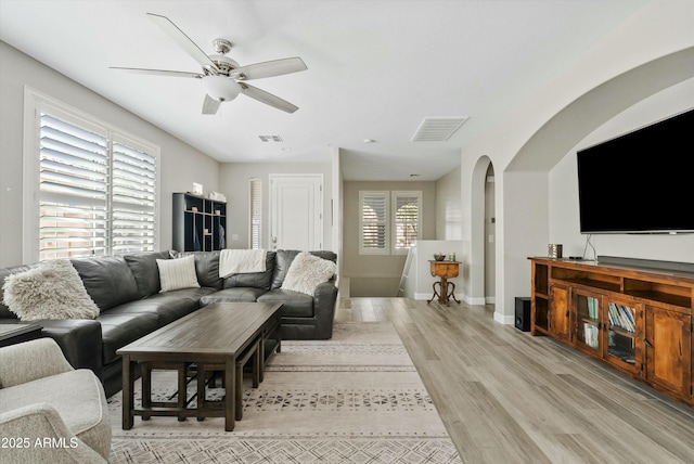 living room featuring light wood-style flooring, visible vents, arched walkways, and baseboards