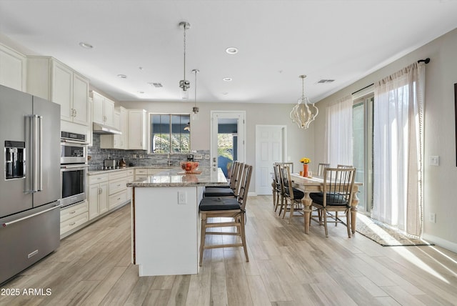 kitchen with appliances with stainless steel finishes, decorative light fixtures, a center island, light stone countertops, and backsplash