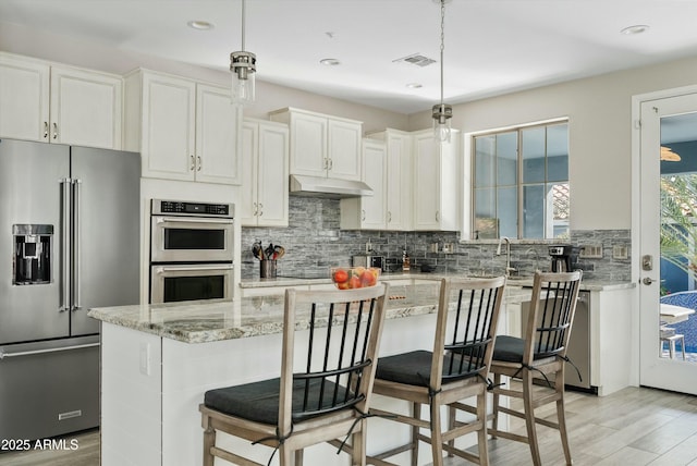 kitchen featuring pendant lighting, light stone counters, white cabinets, and appliances with stainless steel finishes