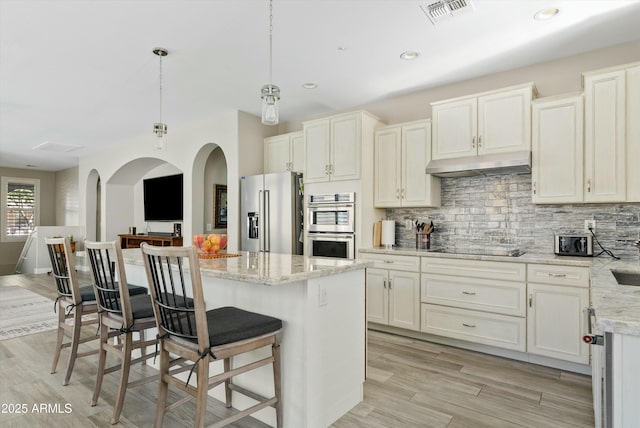 kitchen featuring hanging light fixtures, a kitchen island, stainless steel appliances, light stone countertops, and decorative backsplash