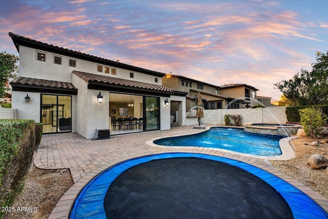 back house at dusk featuring a swimming pool with hot tub, a patio, and pool water feature