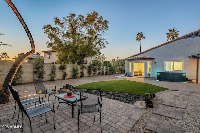 patio terrace at dusk with a yard and a hot tub