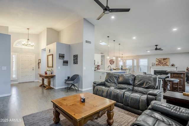 living room featuring sink, ceiling fan with notable chandelier, high vaulted ceiling, and light wood-type flooring