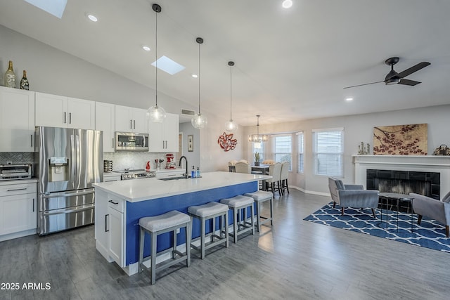 kitchen featuring decorative light fixtures, white cabinets, a kitchen breakfast bar, stainless steel appliances, and a center island with sink