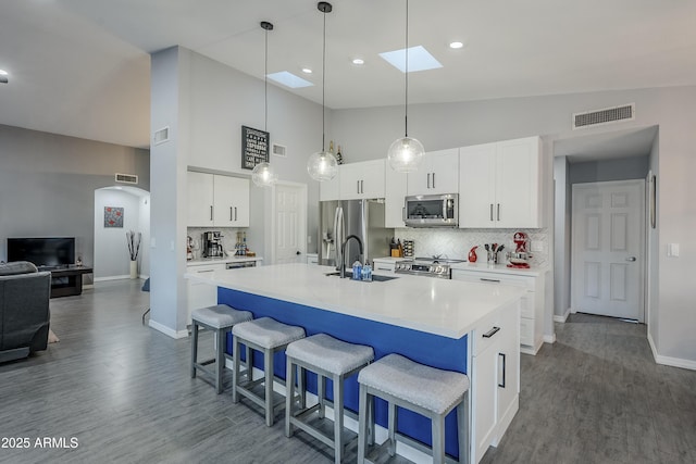 kitchen featuring stainless steel appliances, white cabinetry, pendant lighting, and a center island with sink