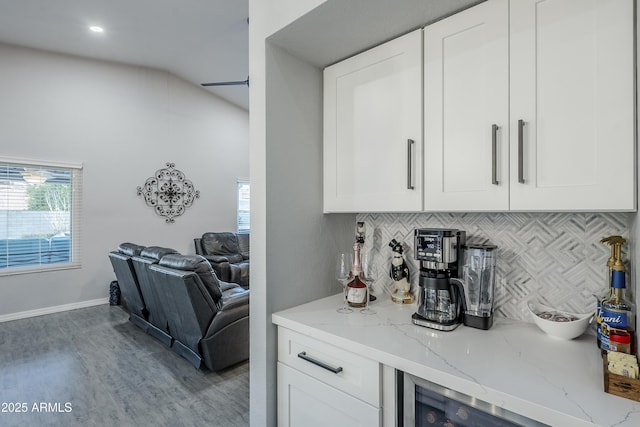 bar with white cabinetry, light stone counters, light hardwood / wood-style floors, and decorative backsplash