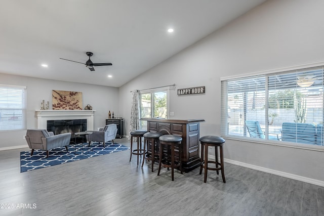 dining area featuring high vaulted ceiling, indoor bar, hardwood / wood-style flooring, ceiling fan, and a tiled fireplace