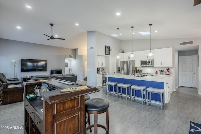 kitchen featuring appliances with stainless steel finishes, a kitchen breakfast bar, white cabinets, a center island with sink, and decorative light fixtures